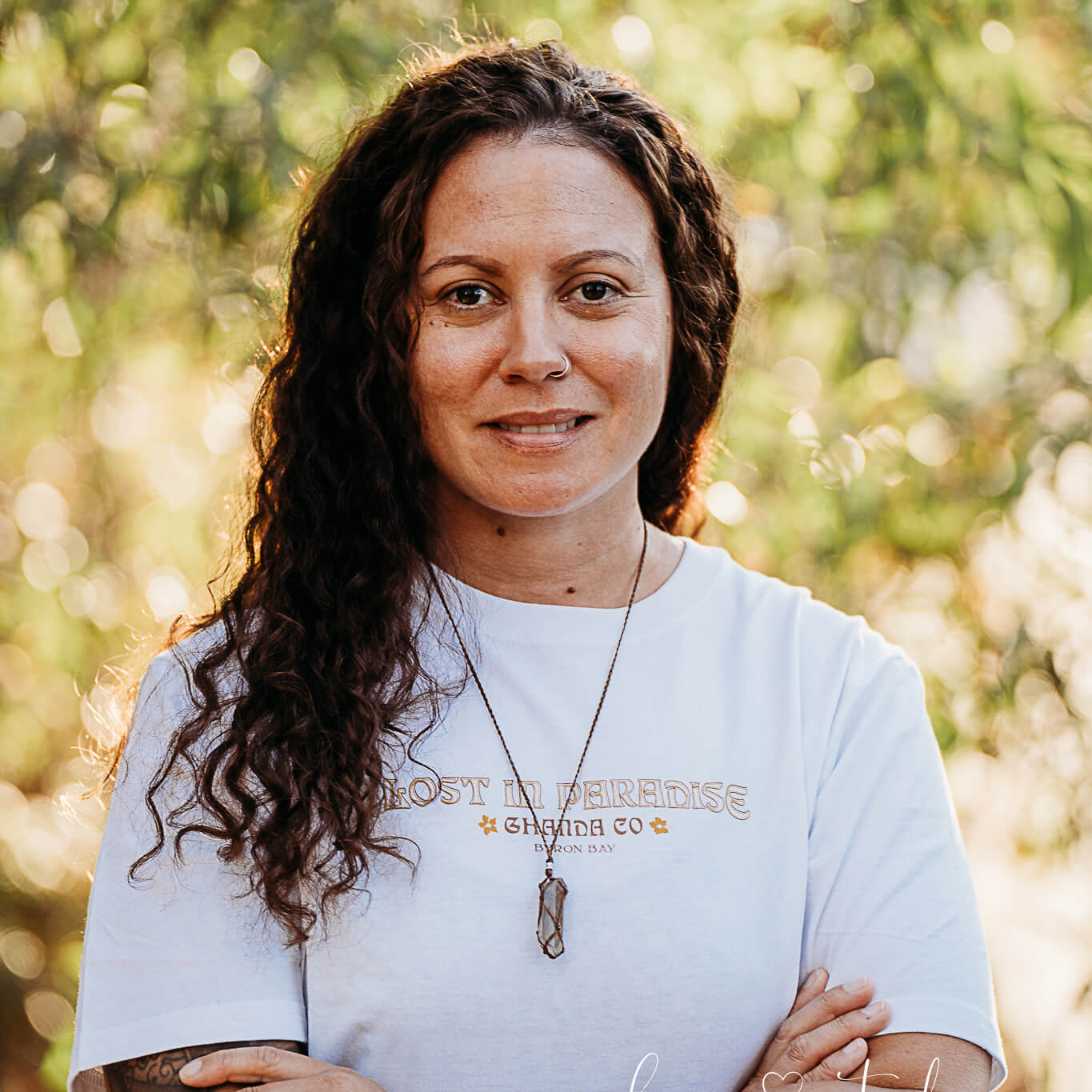 Indigenous artist and Gubbi Gubbi-based woman Chloe Watego smiles for the camera. She has long brown hair and is wearing a white t-shirt.