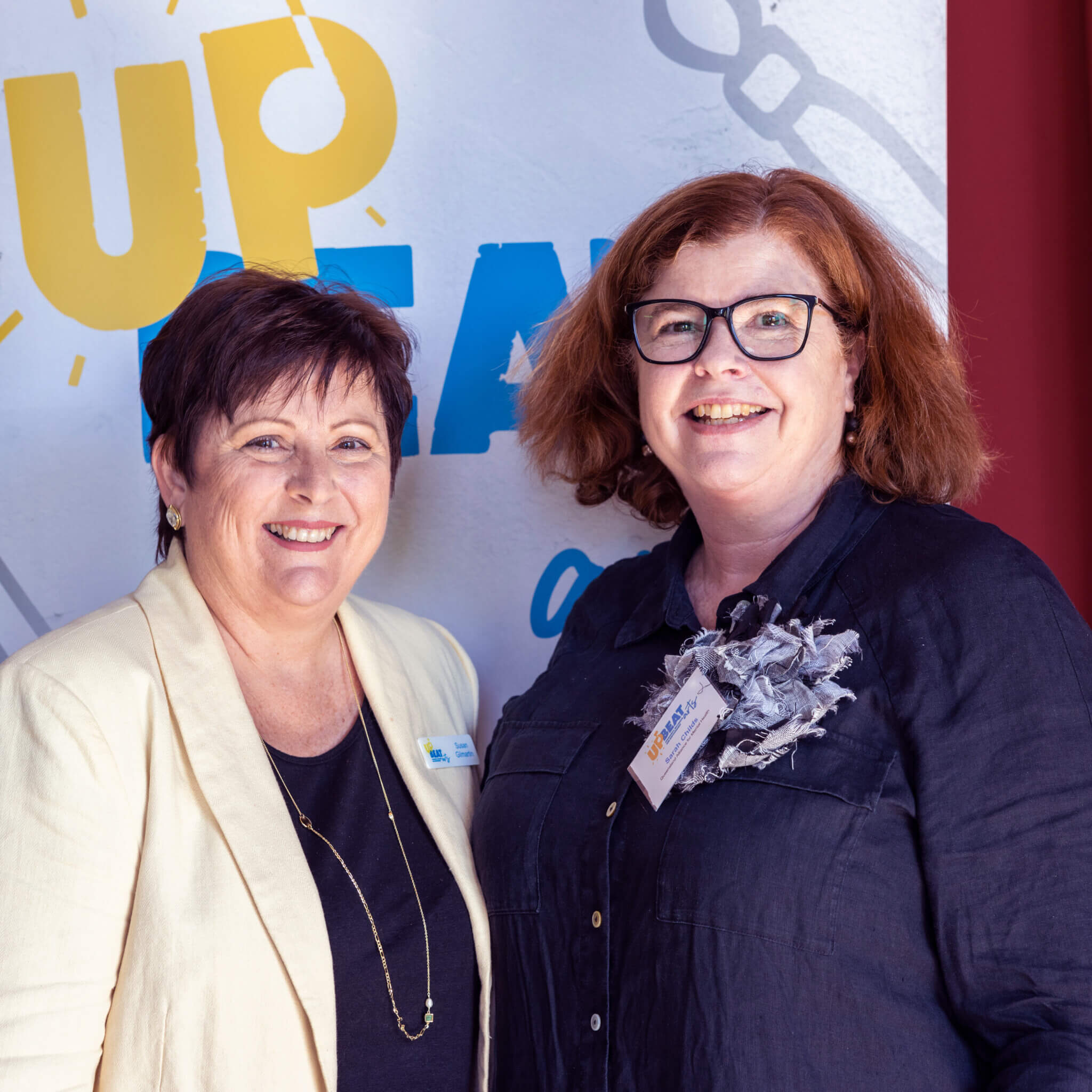 Two of our women members smile for the camera. The woman on the left has short red hair, and wears a cream blazer over a navy top. The woman on the right has shoulder length red hair and wears glasses and a navy shirt.